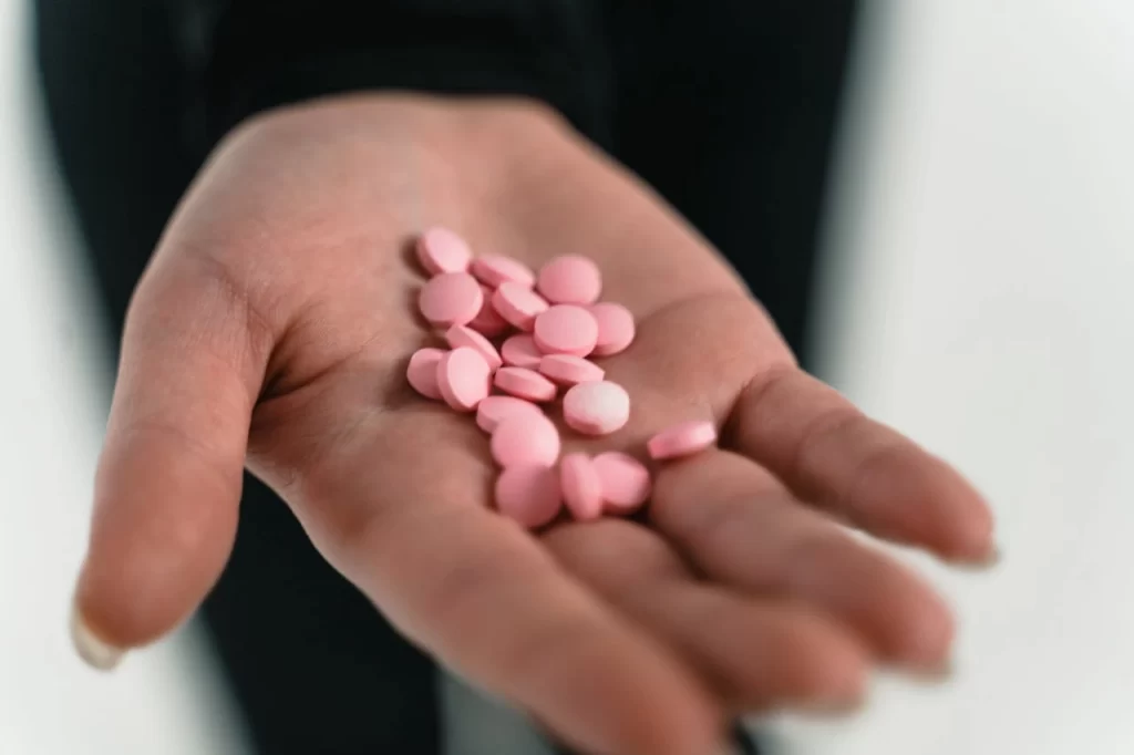 A hand holding pink pills, highlighting the dangers of drug misuse and the importance of professional detox help in London.